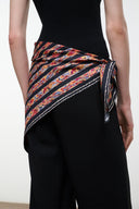Silk scarf with multicolor geometric stripe pattern, tied at waist over dark pants