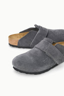 A pair of gray suede clogs with a hook-and-loop strap closure, a cork midsole, and a black outsole, shown on a clean white background.