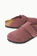 A pair of women's clogs in dusty rose suede with a hook-and-loop strap and a natural cork footbed, shown on a clean white background.
