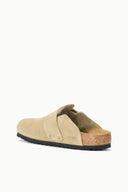 A single beige suede clog shoe with a cork footbed and black sole, shown from a side-rear angle on a clean white background.