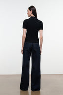 A model shown from the back wearing a black short-sleeve polo shirt and dark wide-leg jeans, standing against a plain white studio wall.