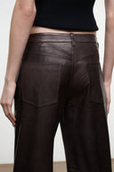 Dark brown leather pants close-up, stitched yoke seam and back pockets.