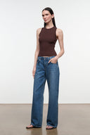 A woman modeling a sleeveless dark brown ribbed top and wide-leg blue jeans against a clean white studio background.