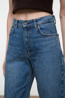 Close-up of a person wearing medium-wash blue denim jeans with a cropped dark brown top visible at the waist.