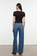 A woman shown from the back wearing a dark brown short-sleeve top and blue wide-leg jeans, standing against a plain white studio wall.