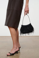 Black mini handbag with long fringe trim and short top handle, side view.