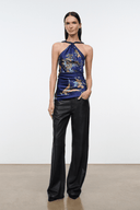 A model stands in a studio wearing a halter-neck satin top with a blue, gold, and green floral print, paired with dark brown wide-leg satin pants.