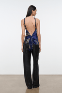 A model is shown from the back wearing a dark brown wide-leg pants jumpsuit with a blue and green patterned open back top, set against a plain white studio background.