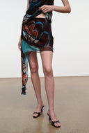 Mini skirt with uneven hem and sheer trailing panel; dark butterfly pattern with teal highlights.