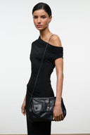 Black convertible shoulder bag with adjustable strap and front flap, held by model