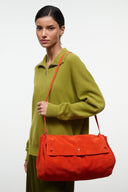 Oversized shoulder bag in tangerine-orange suede with top flap and long strap.