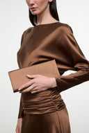 Brown satin clutch in hand with draped long-sleeve dress, ruched waist.