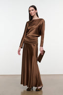 Full-length view of brown satin dress with ruched waist; holding small clutch.