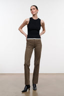 A model stands in a studio wearing a black sleeveless top, brown straight-leg pants, and black ankle boots against a plain light background.