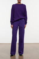 A model wearing a matching purple lounge set consisting of a crewneck sweatshirt and wide-leg trousers, standing against a plain white wall.