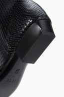 Black snake-embossed flat ankle boot heel close-up with logo on outsole