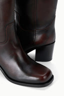 Close-up of dark leather knee-high boots with stitched panel and block heel