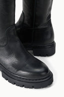Black tall leather boot detail with stitched ankle seam and lug tread sole