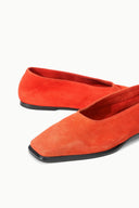 Pair of orange suede flat slip-on shoes, angled side view with black sole