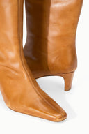 Cashew distressed knee-high leather boot, side view with pointed toe and low heel