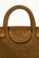 Cigar-brown handbag front with STAUD logo on circular patch beneath the handle.