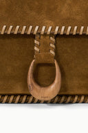 Harlow messenger bag close-up: cigar-brown suede flap with circular buckle hardware