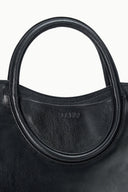 Maude black satchel close-up: oval handle base with stamped logo