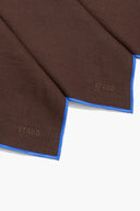 Dark brown linen placemat corners with blue edging and 'STAUD' label